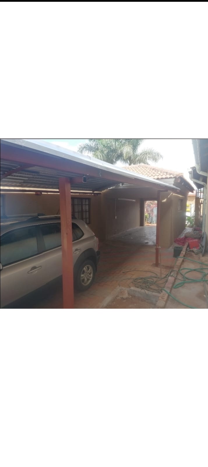 Carport on red steel posts sheltering a parked car